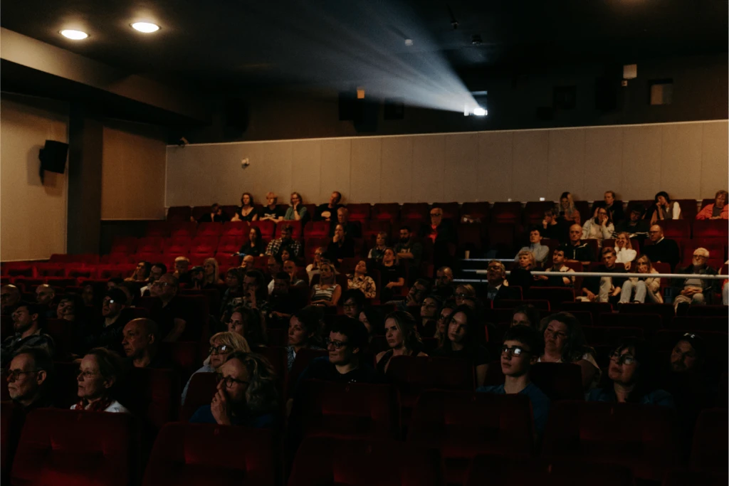 Audiences sit in red chairs watching the screen.