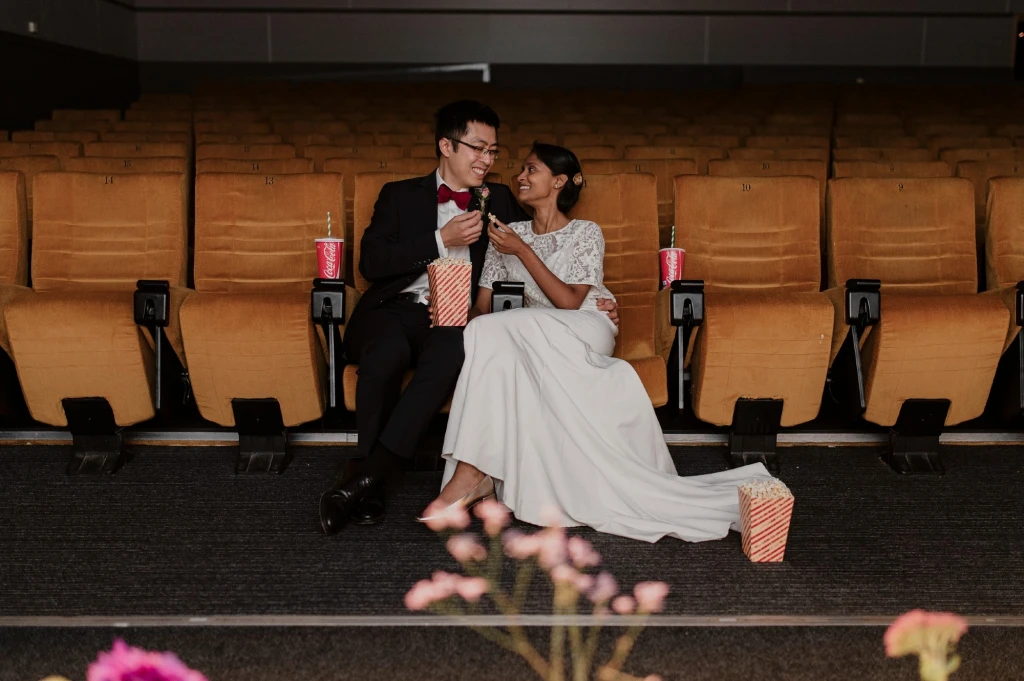A newly-married couple sat in a cinema, eating popcorn together.