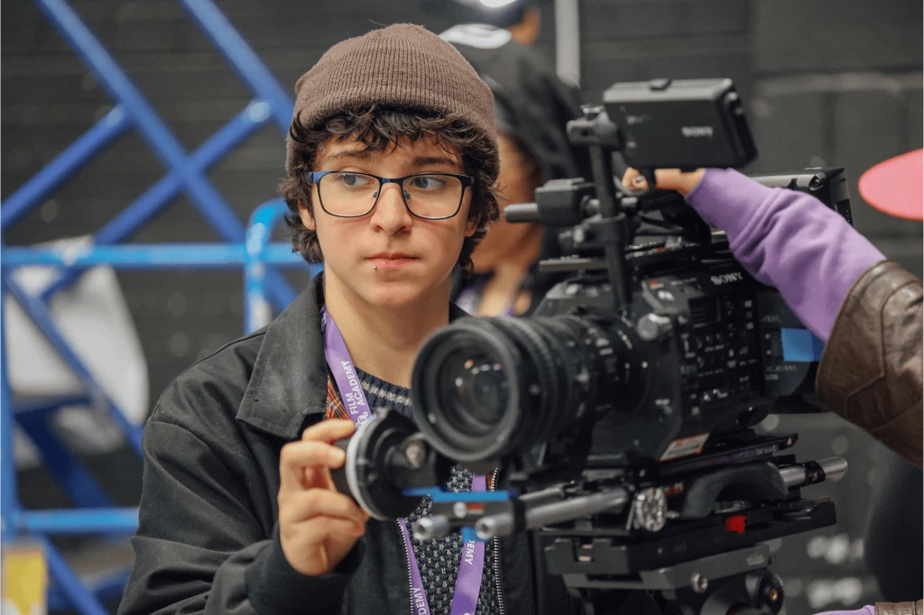 A young person with glasses and a hat operating a camera.