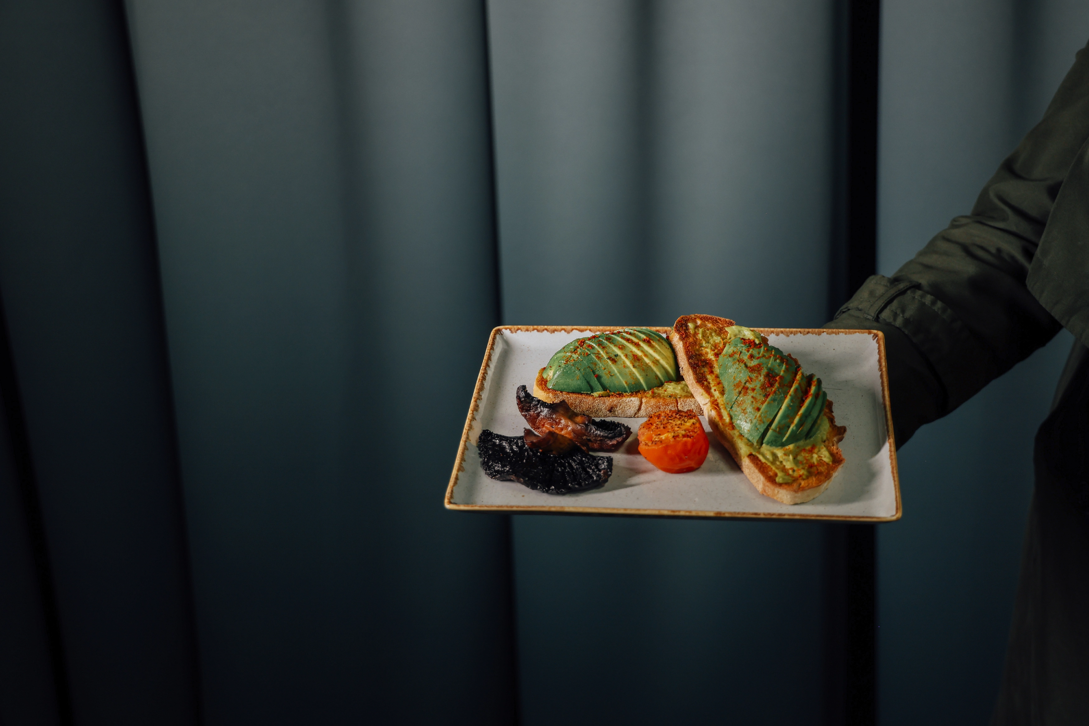 A plate of avocado on toast with tomato and mushroom.