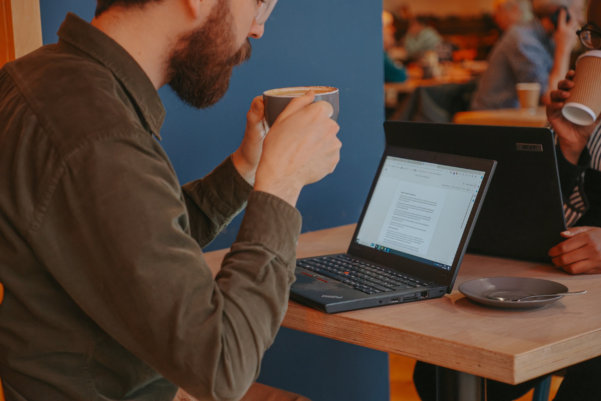 A person working on a laptop, drinking coffee.