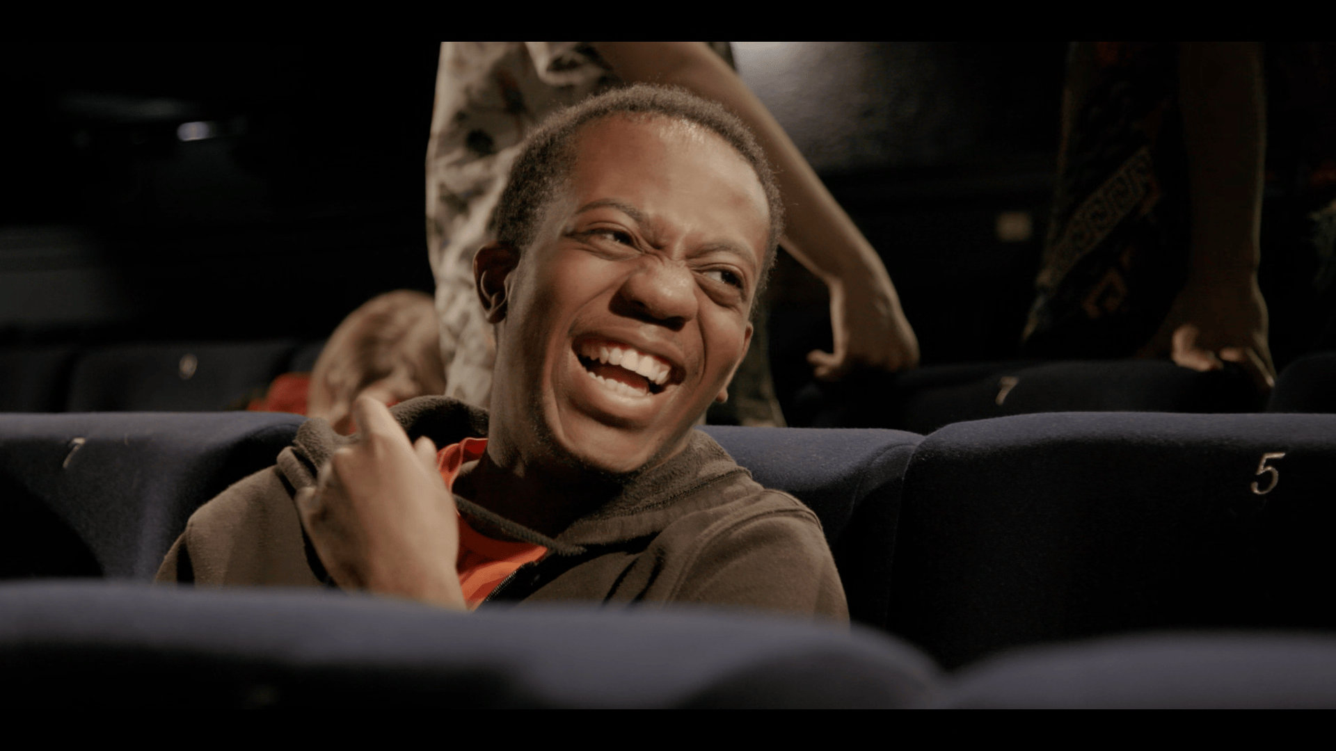 Young man looks to the side laughing as he sits in cinema seats
