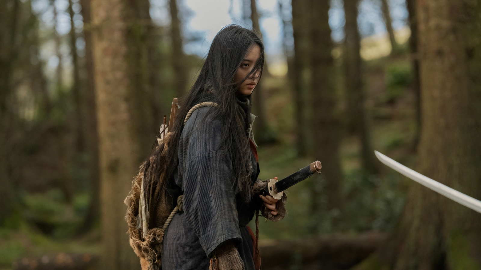 a young woman stands assertively with a samurai sword in a holster o nher hip