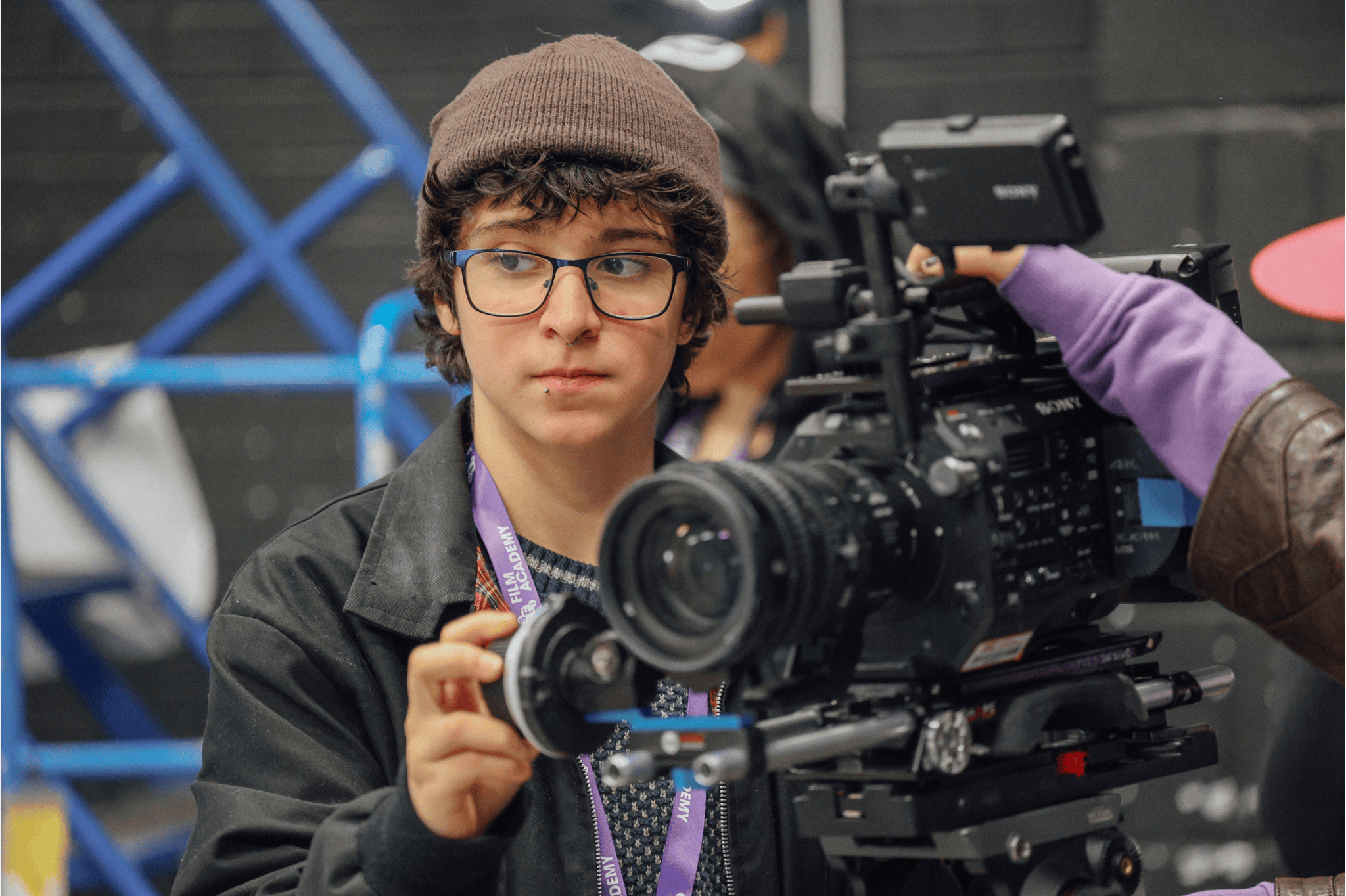 A young person with glasses and a hat operating a camera.